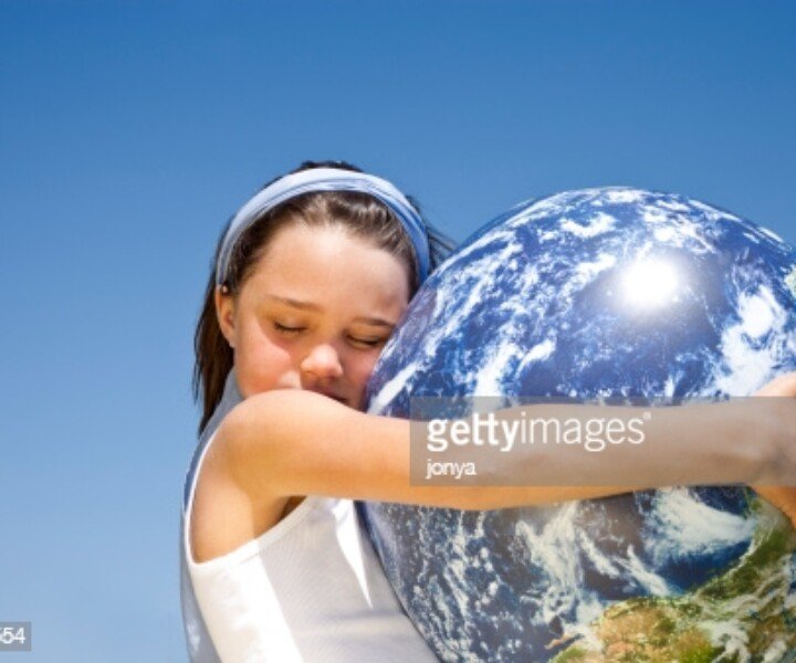 little girl holding globe in her arms, eyes closed, against blue sky